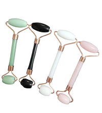 Four facial rollers with different colored stones on a dark background
