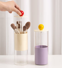 Two cylindrical containers with brushes and a lemon, against a white curtain background.