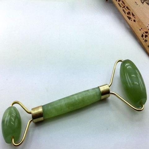 Green jade roller with gold accents on a white surface