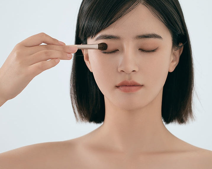 Woman applying makeup with a brush on a plain background