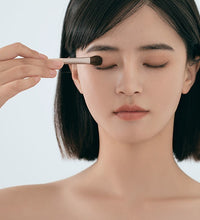 Woman applying makeup with a brush on a plain background