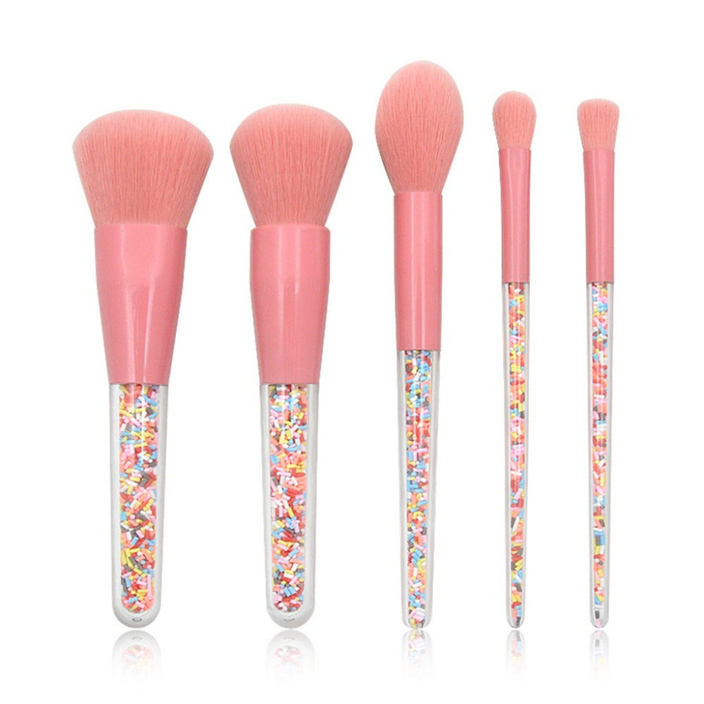 Set of five makeup brushes with pink handles and colorful sprinkles in the handles on a white background