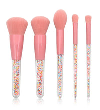 Set of five makeup brushes with pink handles and colorful sprinkles in the handles on a white background