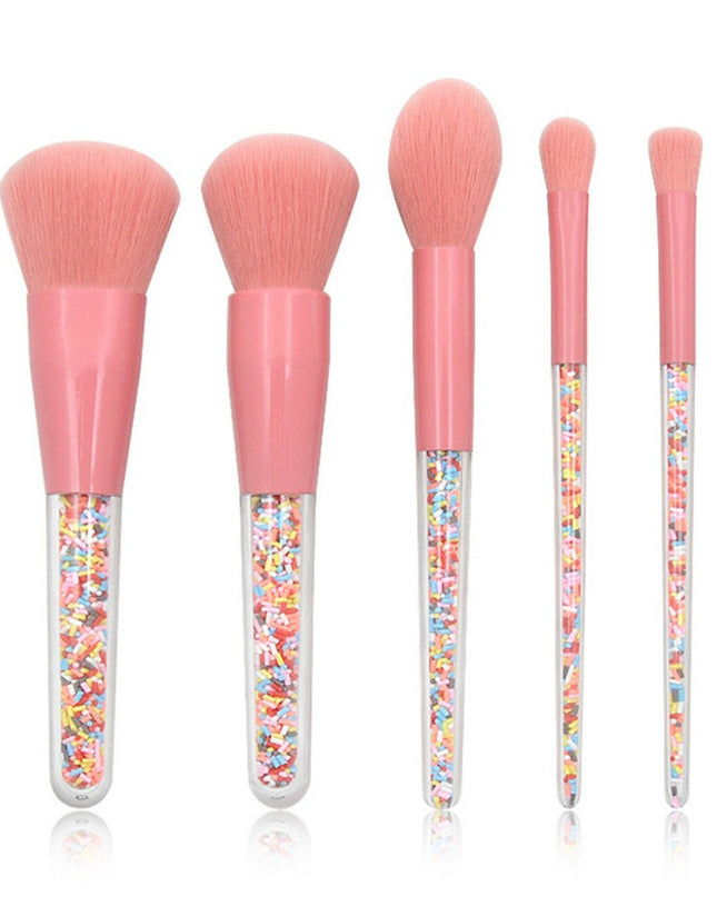 Set of five makeup brushes with pink handles and colorful sprinkles in the handles on a white background