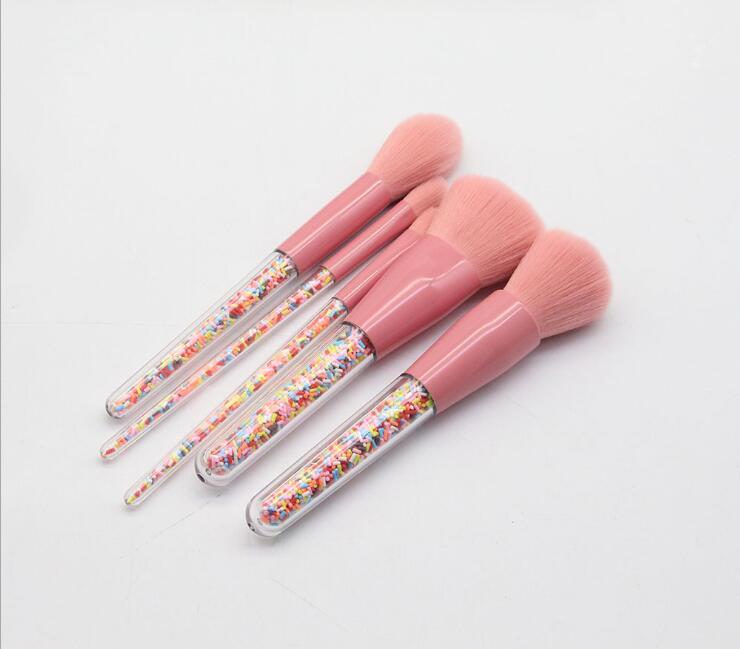 Set of pink makeup brushes with colorful sprinkles on a light gray background