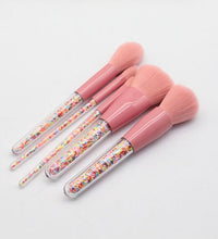 Set of pink makeup brushes with colorful sprinkles on a light gray background